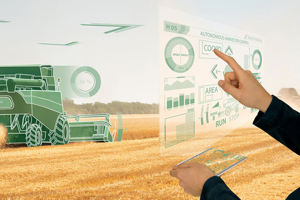 Auf einem halb abgemähten Getreidefeld fährt ein computeranimierter Mähdrescher. Am Rand sieht man die beiden Arme einer Person, die einen virtuellen Screen bedient.
