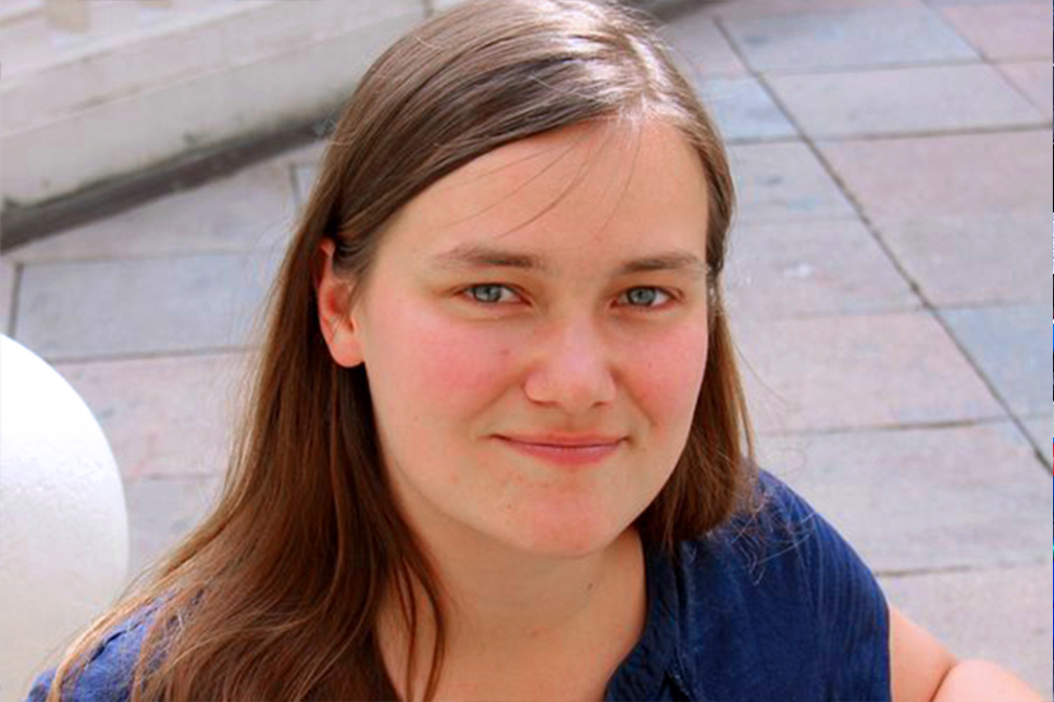 Eine Frau mit langen braunen Haaren blickt in die Kamera und lächelt.