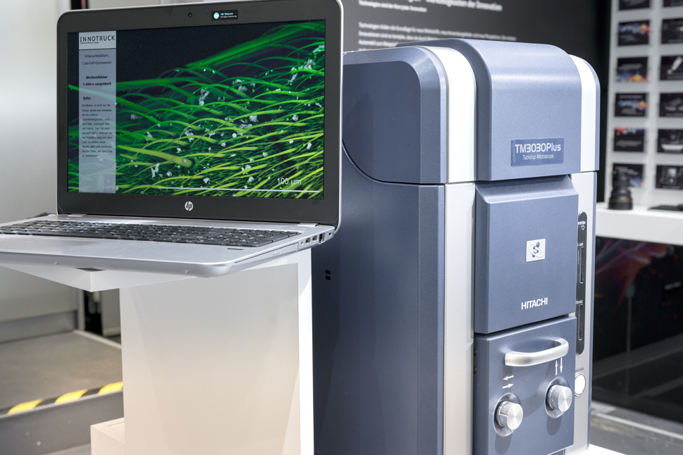 Ein Laptop und das Rasterelektronenmikroskop TM3030Plus von Hitachi, welches aussieht wie ein großer Koffer.