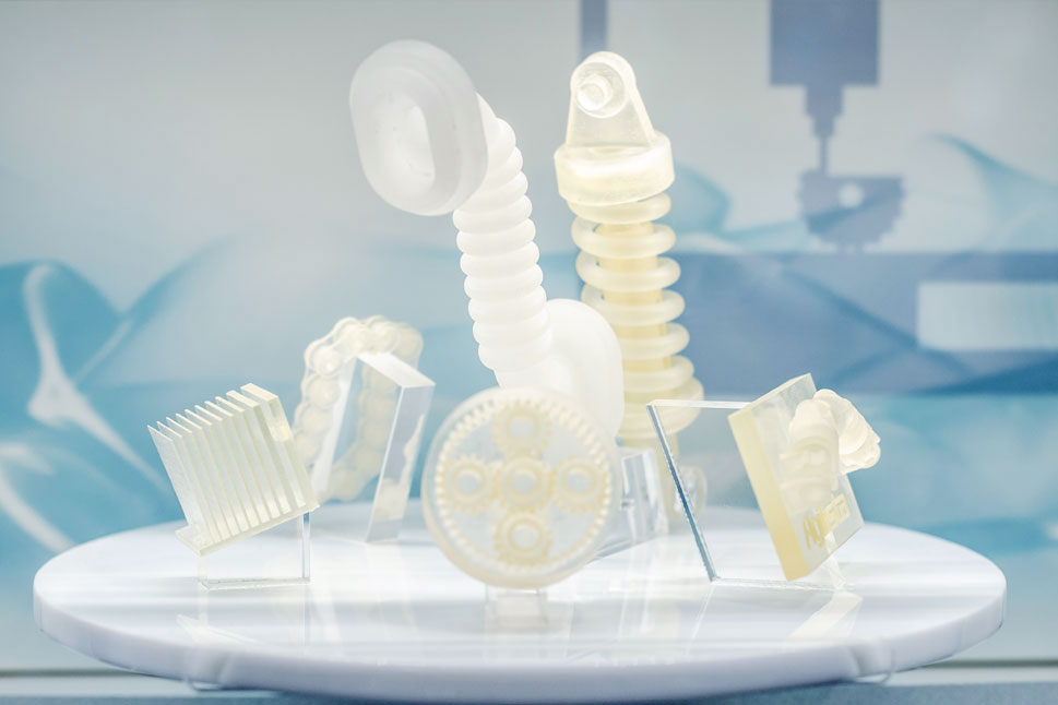 Mehrere kleine Bauteile auf dem 3D-Drucker wie eine Kette, ein Zahnrad oder eine Schraube.