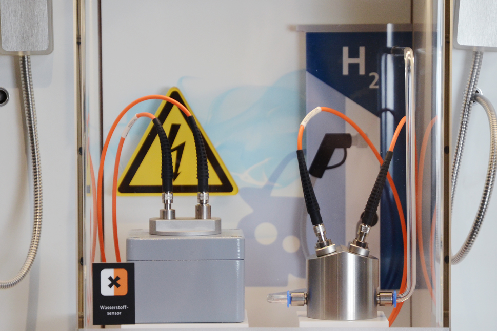 Metallische Boxen aus welchen Kabel herauskommen. Im Hintergrund ein Schild, das vor elektrischem Strom warnt.