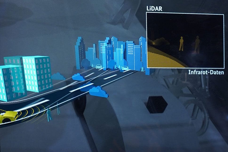 In einer Simulation fährt ein Auto eine Straße mit Bäumen, Häusern und Passanten entlang. Auf einem separaten Bild werden die Infrarot-Daten visualisiert.