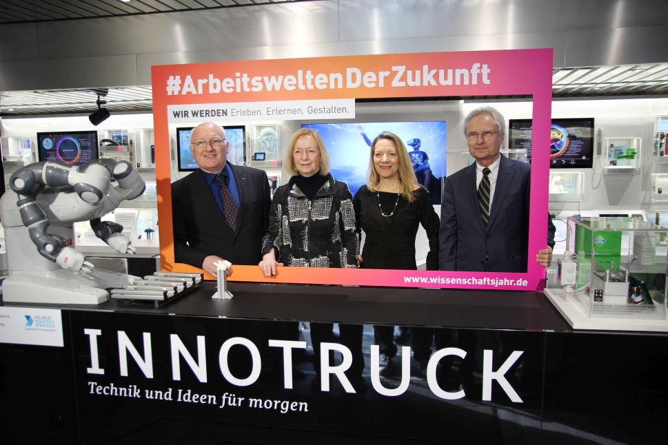 Vier Personen stehen hinter einem Tresen und halten einen Bilderrahmen vor sich.