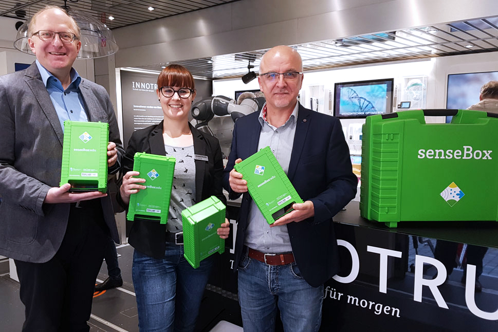 Zwei Männer und eine Frau halten senseBoxen in die Kamera und lächeln freundlich.