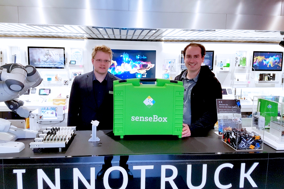 Zwei Männer stehen hinter der Mittelkonsole im InnoTruck, zwischen ihnen steht ein großer grüner Koffer.