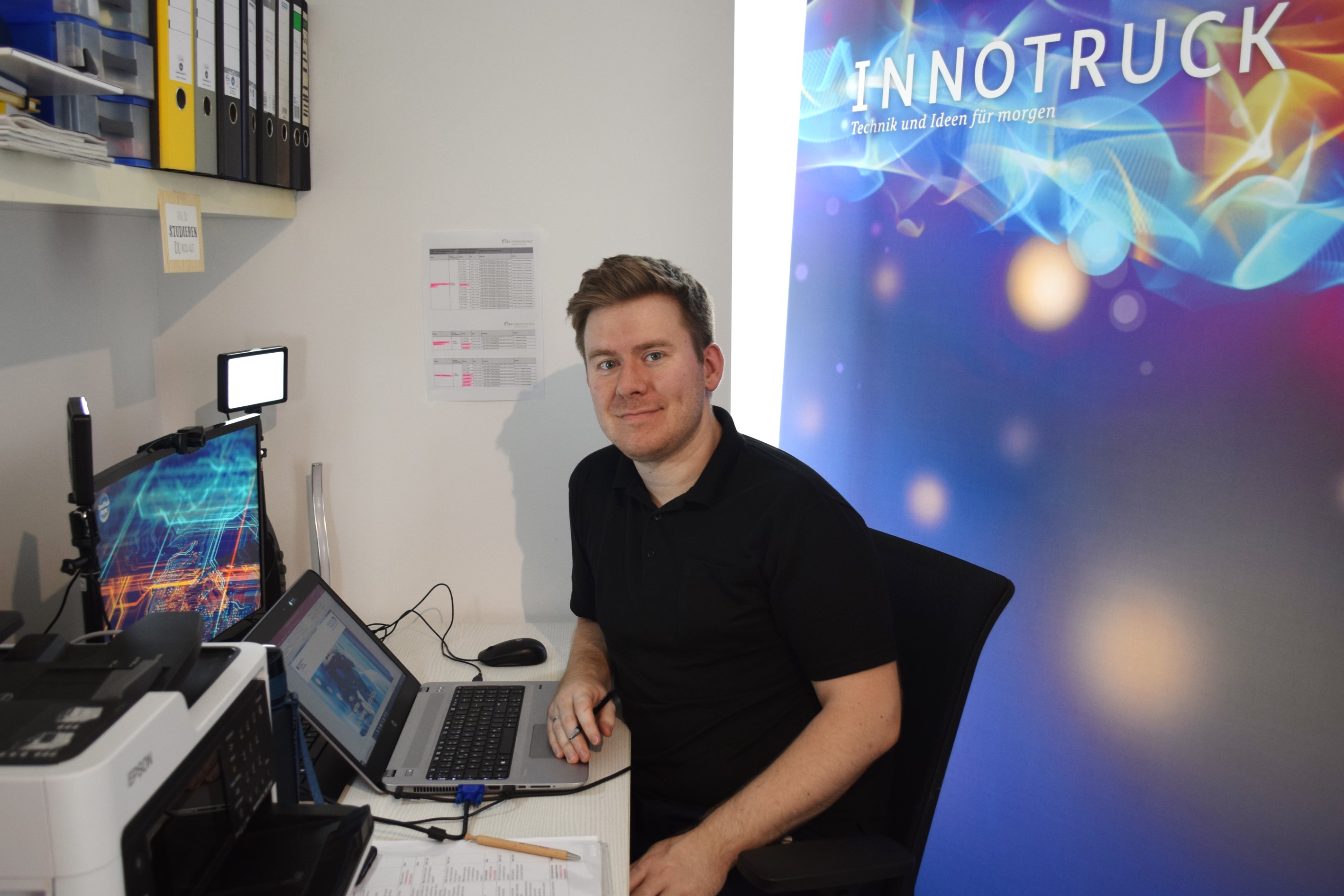 Ein Mann sitzt an einem Schreibtisch mit Bildschirm und Notebook